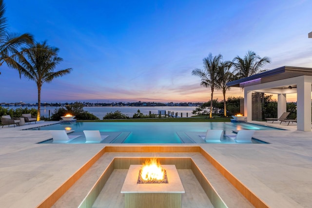 pool at dusk with a patio, a water view, and an outdoor fire pit