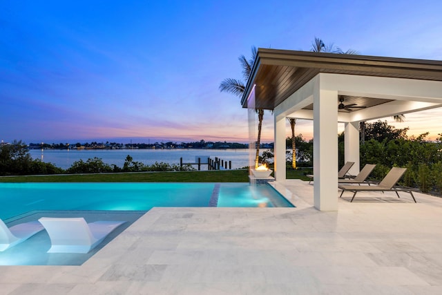 pool at dusk featuring a water view, ceiling fan, a patio, and a gazebo