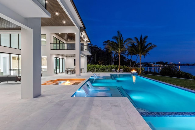 pool at twilight featuring a patio area, pool water feature, and an in ground hot tub