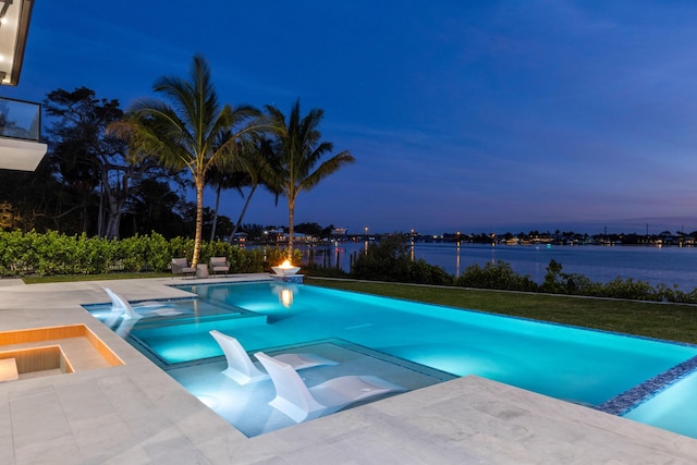 pool at dusk featuring an in ground hot tub, a water view, and a patio