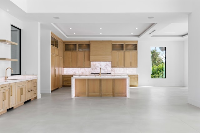 kitchen with tasteful backsplash, wall chimney exhaust hood, a kitchen island with sink, and sink