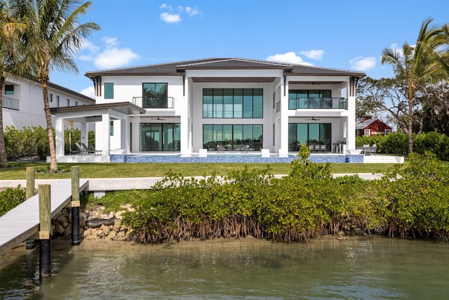 back of property with a water view, a balcony, and ceiling fan