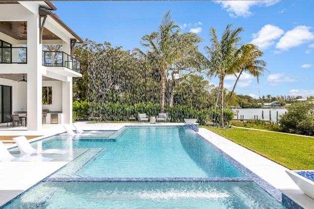 view of swimming pool with a patio, a water view, ceiling fan, and a lawn