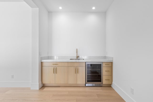 bar featuring sink, light hardwood / wood-style floors, beverage cooler, and light brown cabinets