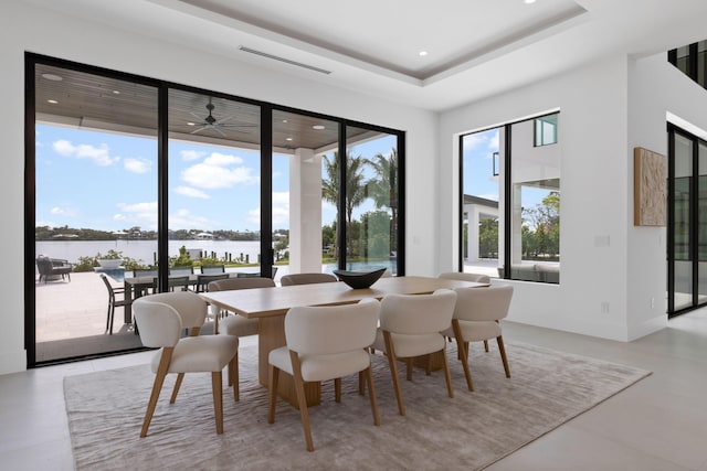 dining area featuring a raised ceiling, a healthy amount of sunlight, and a water view