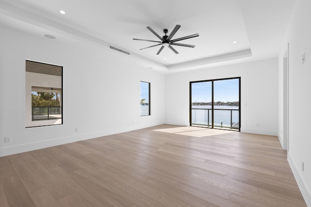 unfurnished room featuring a water view, ceiling fan, a tray ceiling, and light wood-type flooring