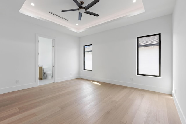 empty room featuring ceiling fan, a tray ceiling, and light hardwood / wood-style flooring