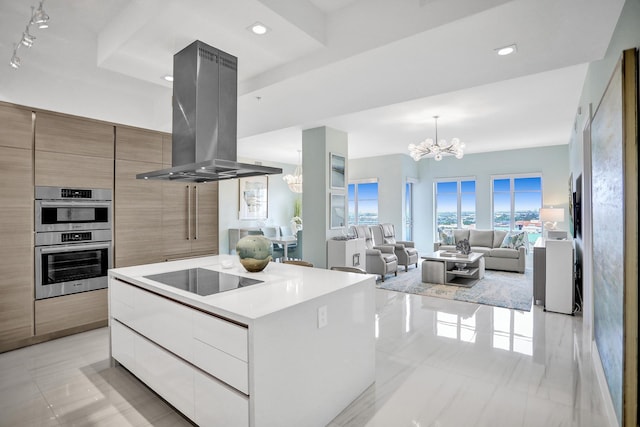 kitchen with island exhaust hood, double oven, white cabinetry, a chandelier, and a kitchen island