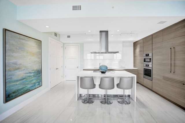 kitchen with stainless steel double oven, island range hood, white cabinets, a center island, and a breakfast bar area