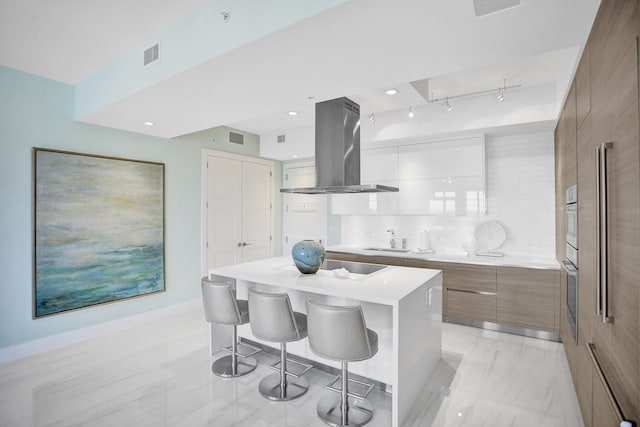 kitchen featuring white cabinetry, a center island, sink, a kitchen breakfast bar, and island range hood