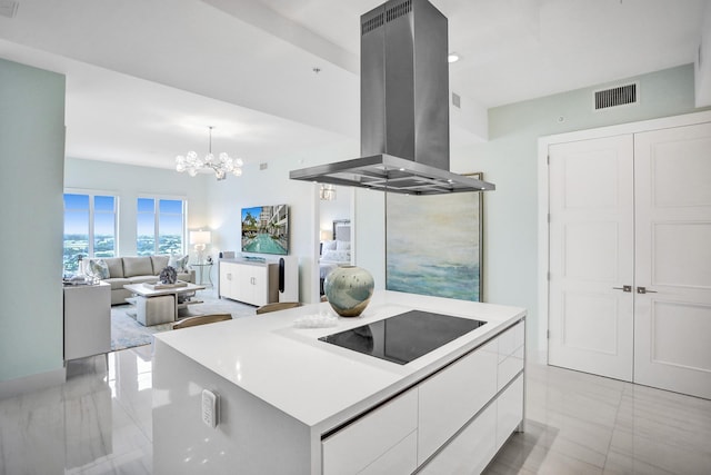 kitchen with island exhaust hood, black electric cooktop, a kitchen island, a notable chandelier, and white cabinetry