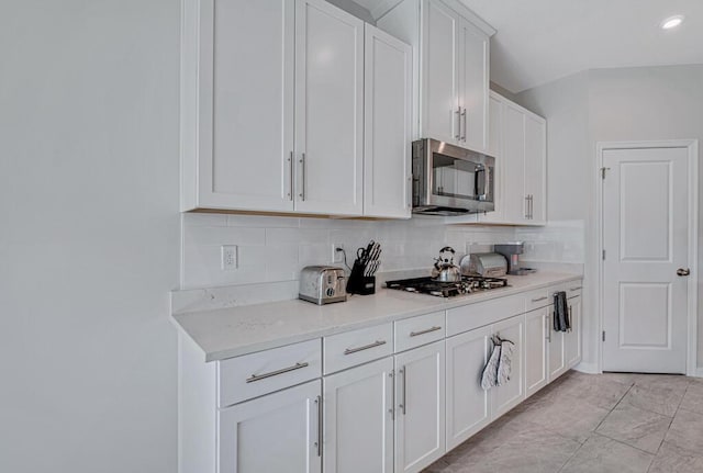 kitchen with white cabinets, decorative backsplash, stainless steel appliances, and light stone countertops