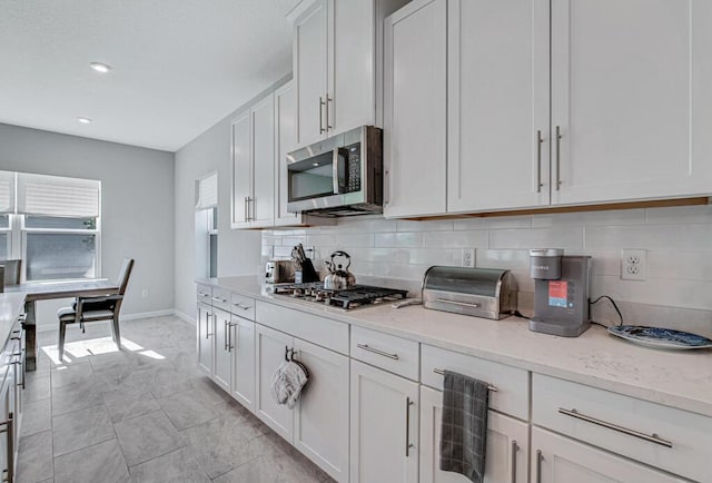 kitchen with backsplash, light stone counters, white cabinets, and appliances with stainless steel finishes