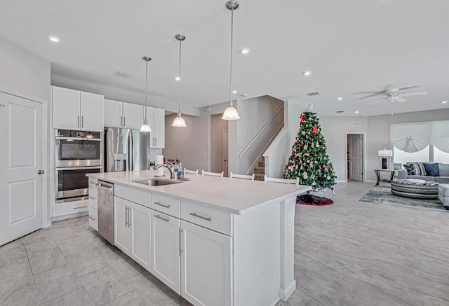 kitchen with sink, stainless steel appliances, pendant lighting, a center island with sink, and white cabinets