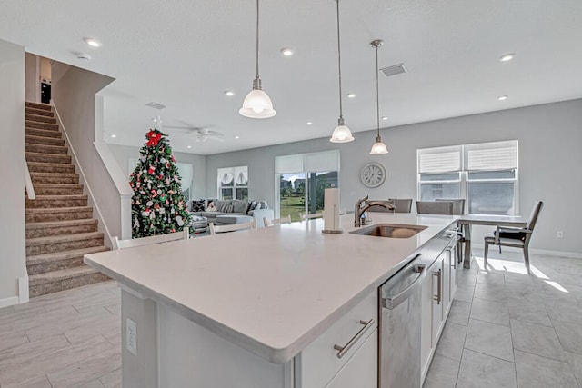 kitchen featuring sink, dishwasher, white cabinets, hanging light fixtures, and an island with sink