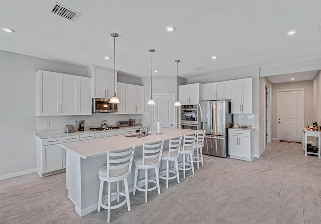 kitchen with backsplash, stainless steel appliances, sink, a center island with sink, and white cabinetry