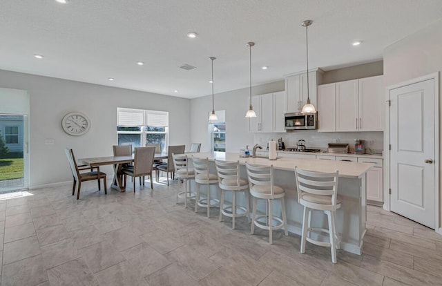 kitchen featuring a center island with sink, hanging light fixtures, decorative backsplash, white cabinetry, and stainless steel appliances