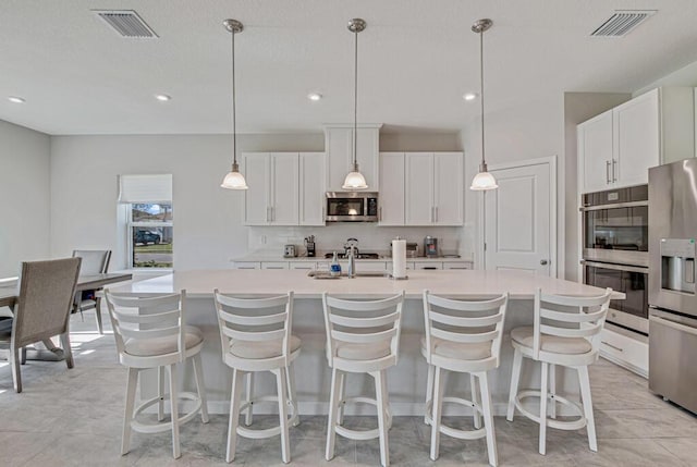 kitchen featuring pendant lighting, stainless steel appliances, white cabinetry, and a kitchen island with sink