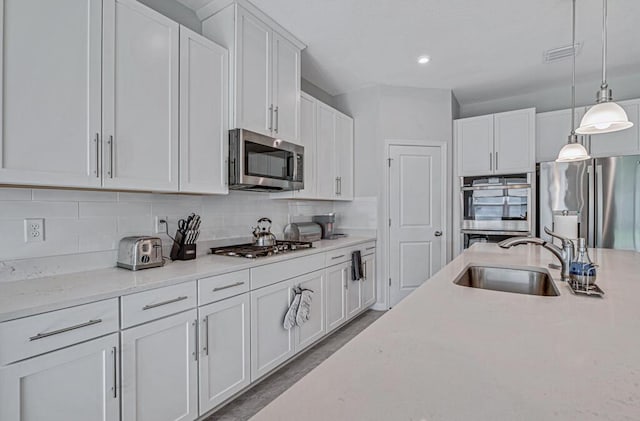 kitchen featuring pendant lighting, white cabinets, sink, light stone counters, and stainless steel appliances