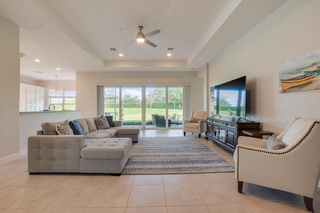 tiled living room with ceiling fan with notable chandelier and a raised ceiling