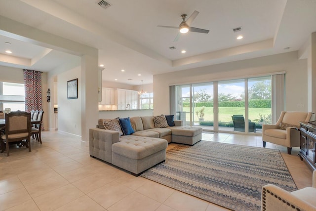 living room with a tray ceiling, light tile patterned floors, and ceiling fan with notable chandelier