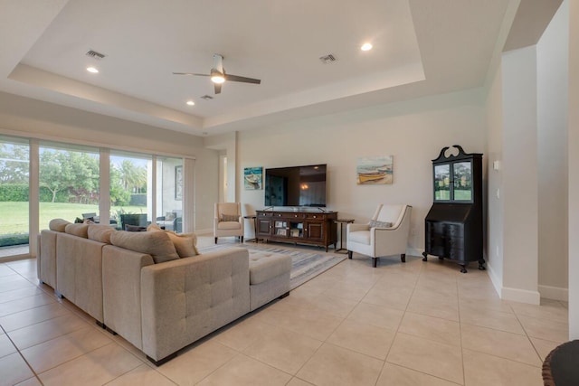 tiled living room with ceiling fan and a tray ceiling