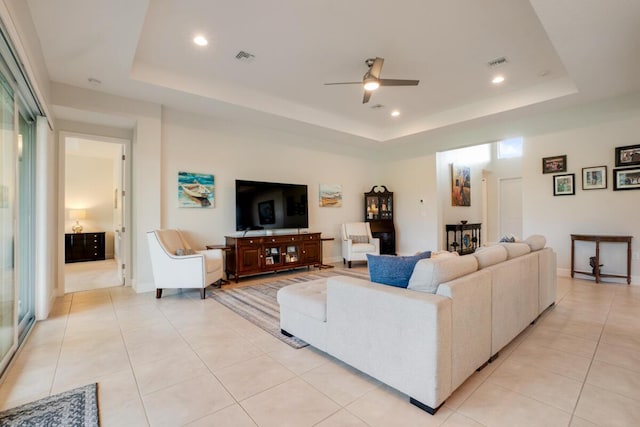 living room featuring a tray ceiling, ceiling fan, and light tile patterned flooring