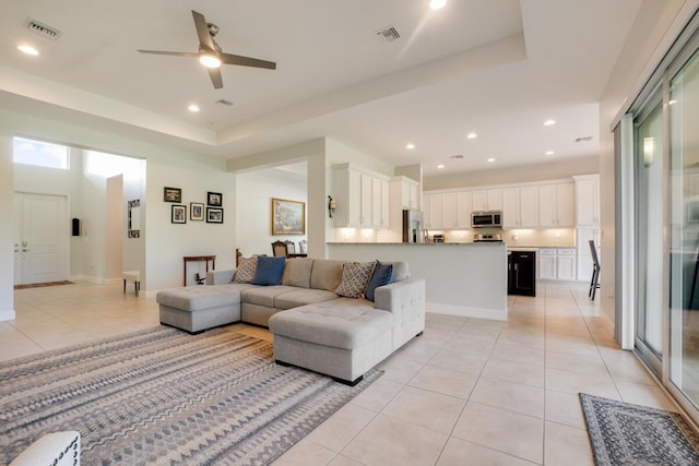 living room with light tile patterned floors, a raised ceiling, and ceiling fan