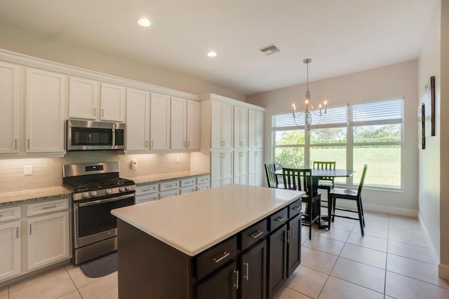 kitchen featuring white cabinets, decorative backsplash, hanging light fixtures, and appliances with stainless steel finishes