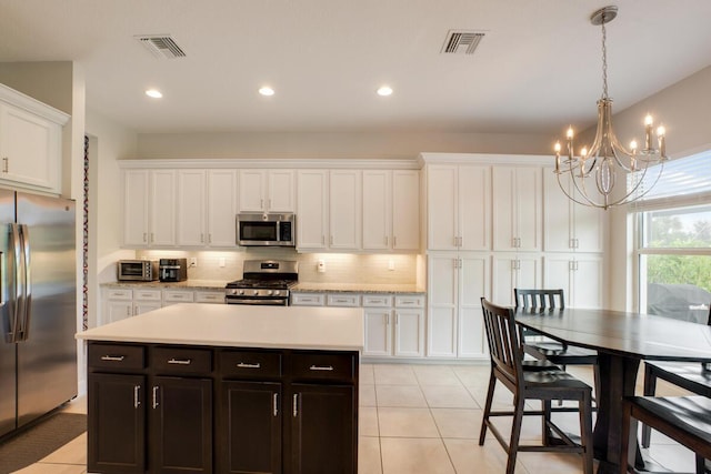 kitchen featuring white cabinetry, stainless steel appliances, light tile patterned floors, a notable chandelier, and a kitchen island