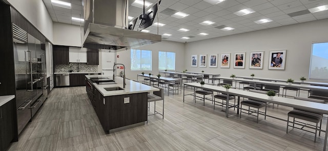 kitchen featuring a breakfast bar, a drop ceiling, a kitchen island with sink, sink, and decorative backsplash