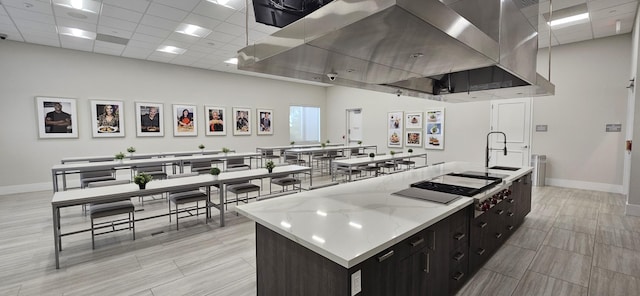 kitchen featuring a paneled ceiling, sink, a large island, stovetop, and light stone counters