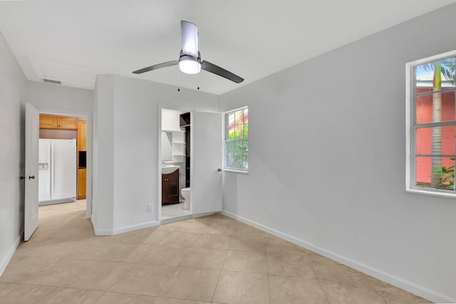 unfurnished bedroom featuring light tile patterned flooring, ceiling fan, white refrigerator with ice dispenser, and multiple windows