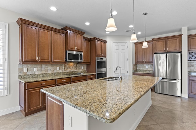 kitchen with pendant lighting, sink, a kitchen island with sink, stainless steel appliances, and light stone counters