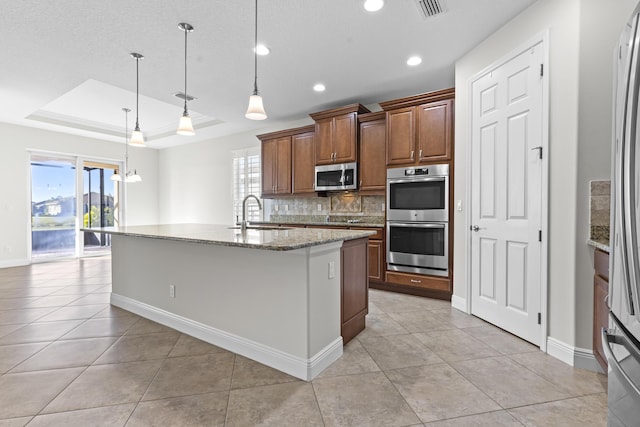 kitchen with sink, appliances with stainless steel finishes, hanging light fixtures, a center island with sink, and a raised ceiling