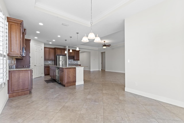 kitchen featuring pendant lighting, stainless steel fridge, ceiling fan, a tray ceiling, and a center island with sink