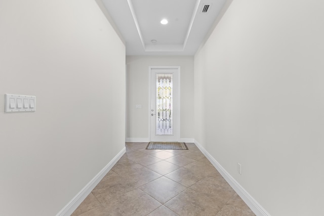 doorway to outside with light tile patterned floors and a raised ceiling