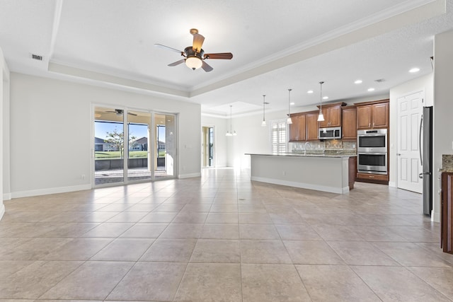 kitchen with pendant lighting, a tray ceiling, a kitchen island with sink, and stainless steel appliances