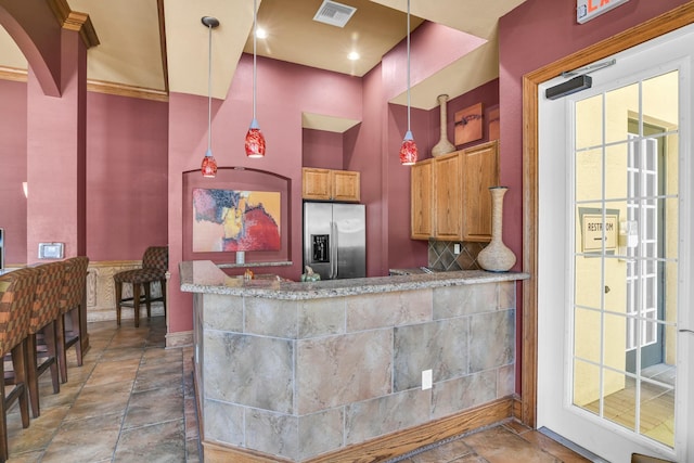 kitchen featuring stainless steel refrigerator with ice dispenser, kitchen peninsula, hanging light fixtures, and light stone countertops