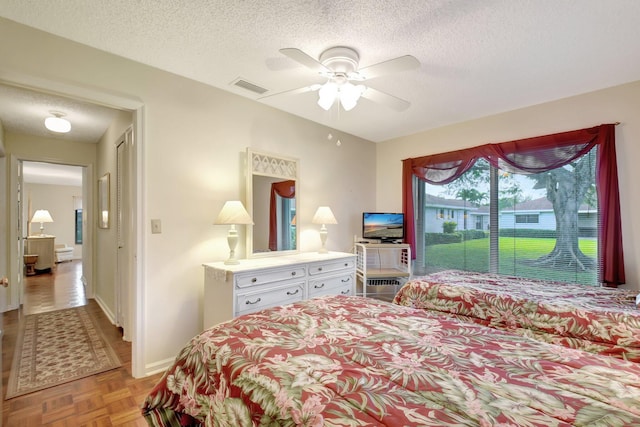 bedroom with ceiling fan, a textured ceiling, and light parquet floors