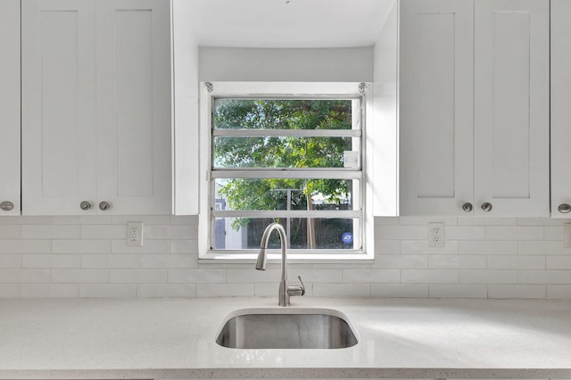 kitchen featuring light stone countertops, white cabinetry, and sink