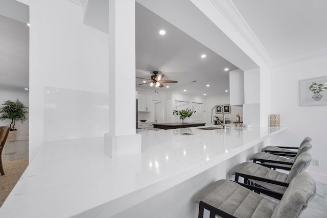 interior space featuring kitchen peninsula, white cabinetry, ornamental molding, and light stone counters