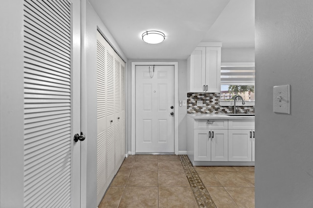 kitchen with decorative backsplash, white cabinetry, sink, and light tile patterned floors