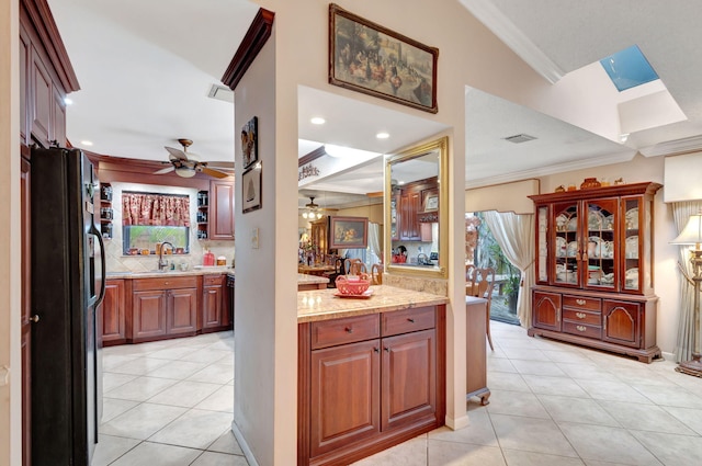 kitchen featuring decorative backsplash, black refrigerator, light tile patterned floors, and crown molding