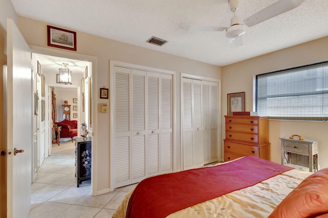 bedroom with a textured ceiling, ceiling fan, multiple closets, and light tile patterned flooring