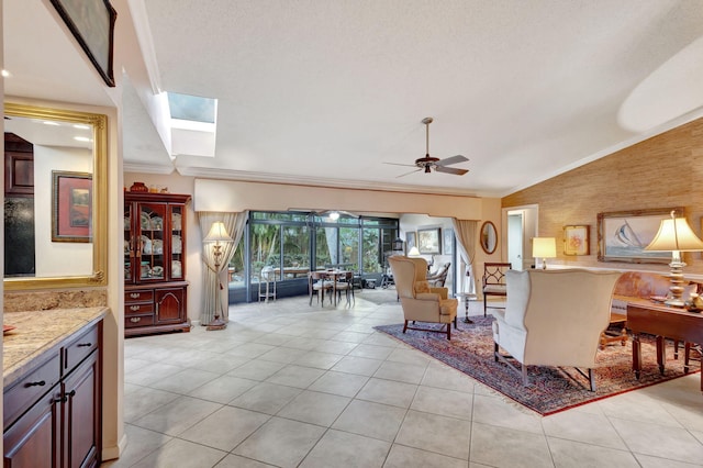 living room featuring vaulted ceiling with skylight, ceiling fan, ornamental molding, a textured ceiling, and light tile patterned floors