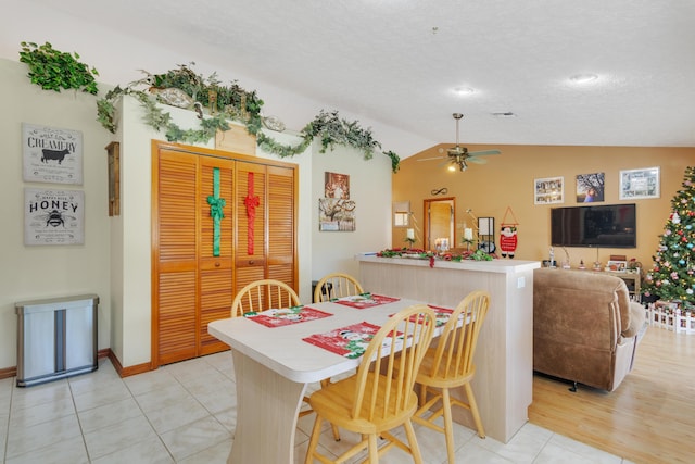 dining room featuring a textured ceiling, ceiling fan, light tile patterned floors, and vaulted ceiling