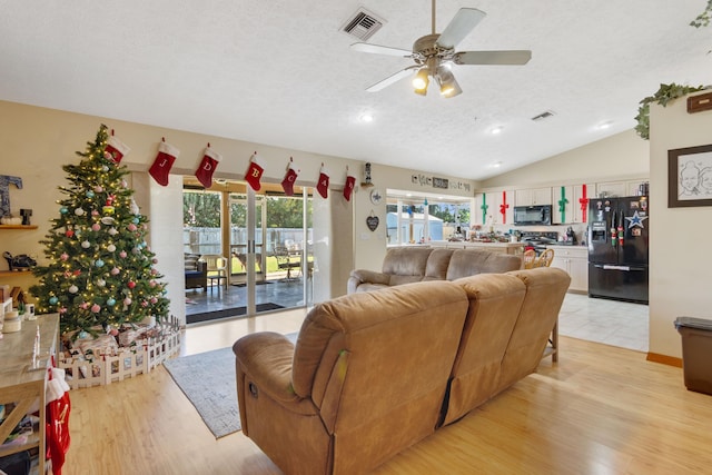 living room featuring ceiling fan, lofted ceiling, a textured ceiling, and light hardwood / wood-style flooring