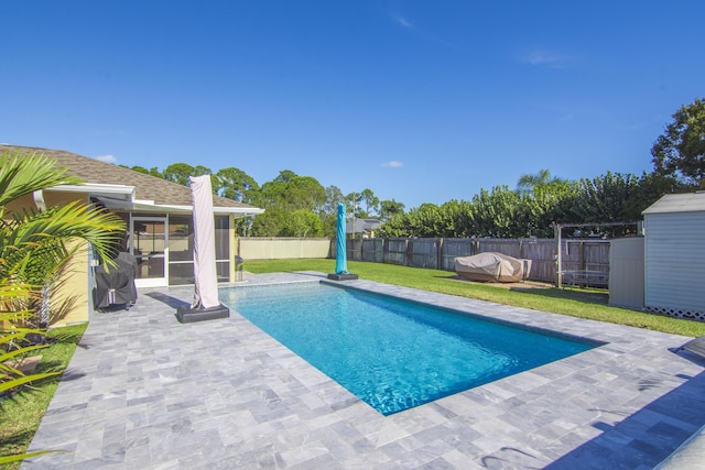 view of swimming pool featuring a sunroom, a yard, a patio, and a shed