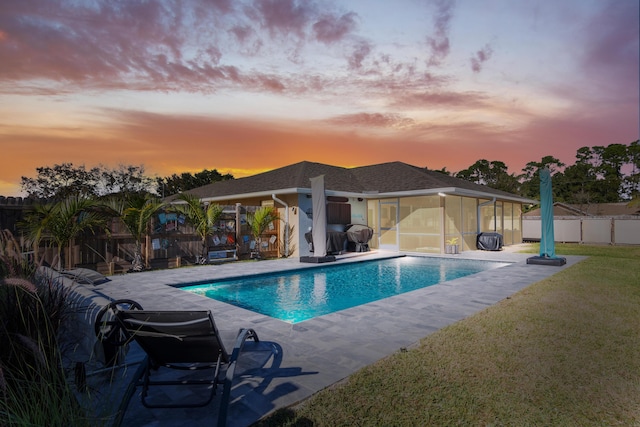 pool at dusk featuring a lawn, a sunroom, and a patio